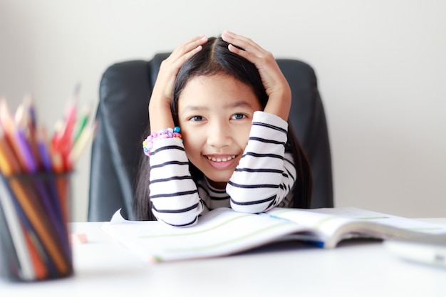 Feliz menina asiática fazendo lição de casa e sorrindo