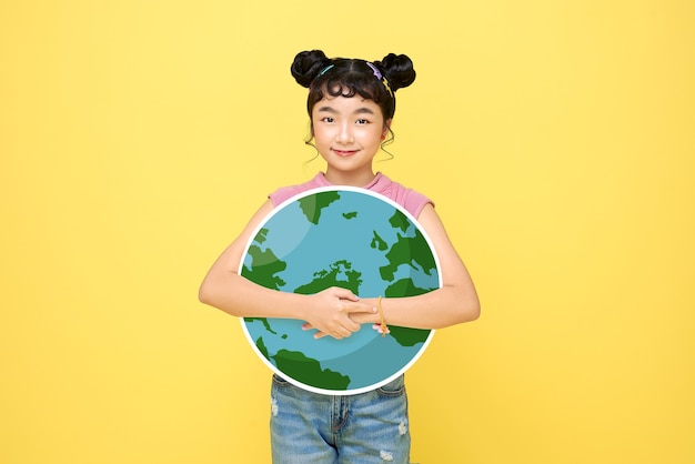 Feliz menina asiática linda colegial abraçar globo isolado em fundo amarelo. conceito do dia do meio ambiente mundial.