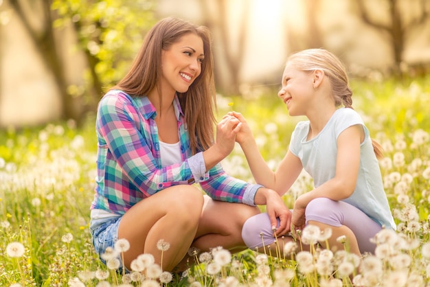 Feliz menina bonitinha com mãe segurando dente de leão no parque.