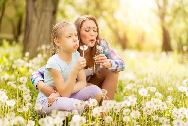 Feliz menina bonitinha soprando dente de leão com a mãe no parque.