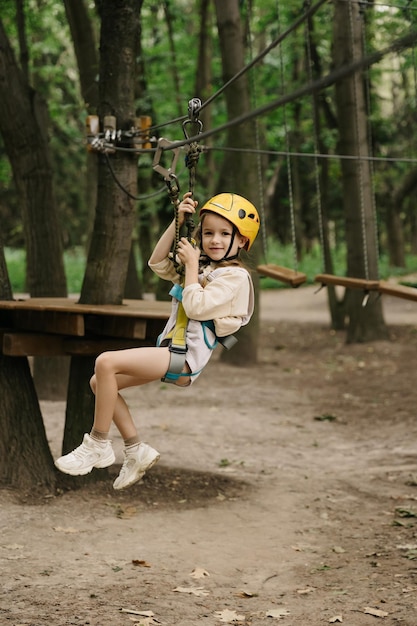 Feliz menina de seis anos em atividade de escalada no parque florestal de arame alto Uma linda menina sobe em um arnês de corda