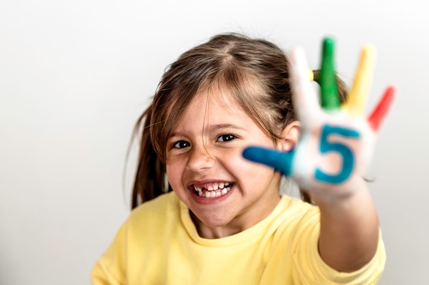 Feliz menina desdentada com o número cinco pintado na mão rindo e se divertindo Menina que está pintando as mãos com números O número cinco e o conceito de infância