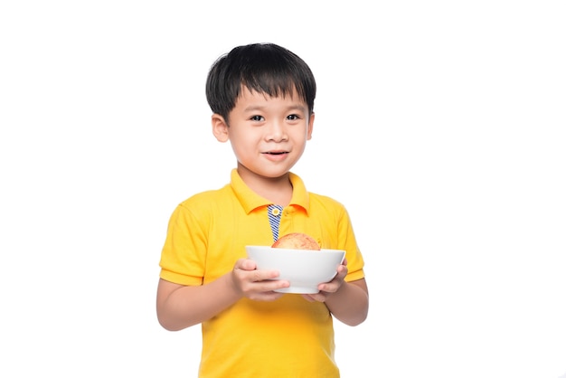 Feliz menino asiático segurando uma maçã vermelha na tigela.