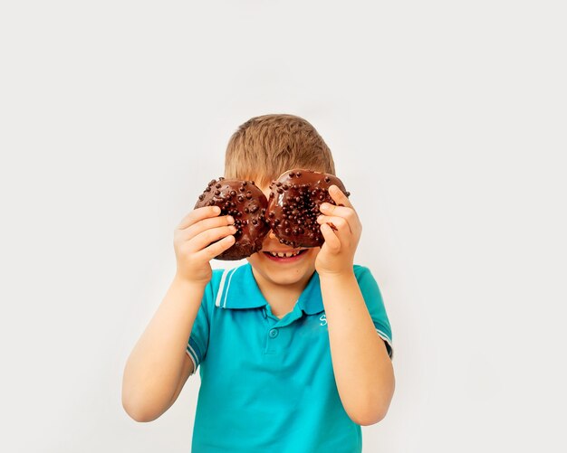 Feliz menino bonito se diverte brincando com donuts em uma parede de luz. Rosquinhas de chocolate