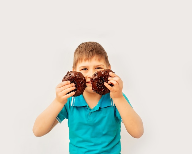 Feliz menino bonito se diverte brincando com donuts em uma parede de luz. Rosquinhas de chocolate