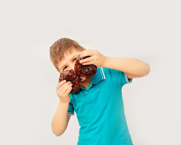 Feliz menino bonito se diverte brincando com donuts em uma parede de luz. Rosquinhas de chocolate