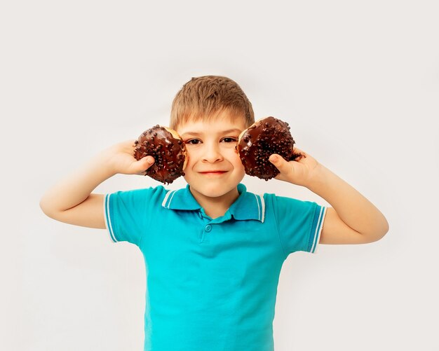 Feliz menino bonito se diverte brincando com donuts em uma parede de luz. rosquinhas de chocolate