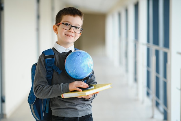Feliz menino inteligente bonitinho de óculos com mochila e livro na mão Primeira vez na escola De volta à escola
