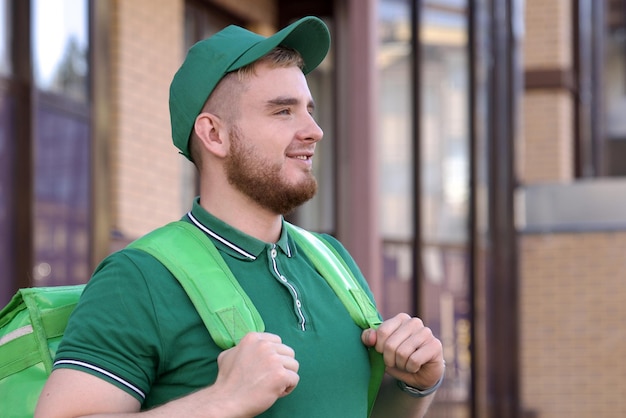 Feliz mensajero joven en uniforme verde con una gran bolsa térmica o mochila entregar comida de