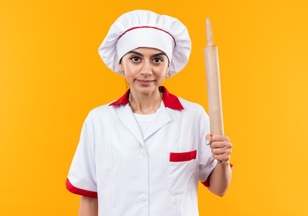 Feliz mirando a la cámara joven hermosa en uniforme de chef con rodillo