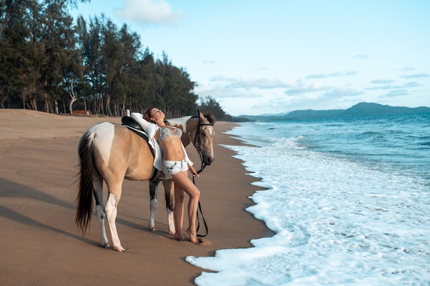 Feliz moda jovem posando com um cavalo na praia