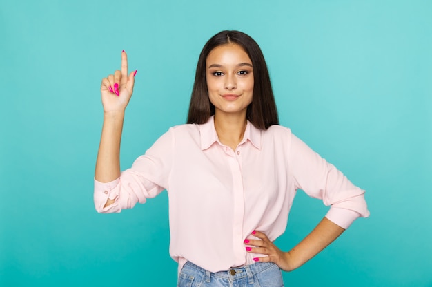 Feliz modelo feminino na blusa branca está na sala azul apontando algo isolado.