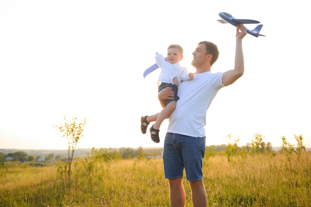 Feliz momento pai filho Pai pegando carona em seu filho ao pôr do sol enquanto ele brinca com avião de brinquedo