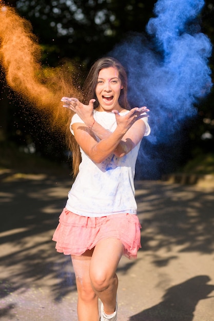 Feliz morena mujer asiática con pelo largo jugando con pintura Holi explotando a su alrededor