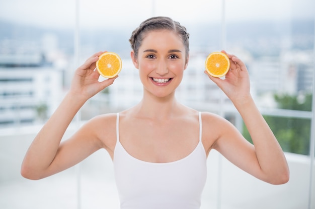 Foto feliz morena saudável segurando fatias de laranja