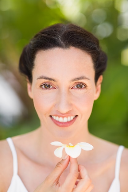 Foto feliz morena sosteniendo una flor blanca