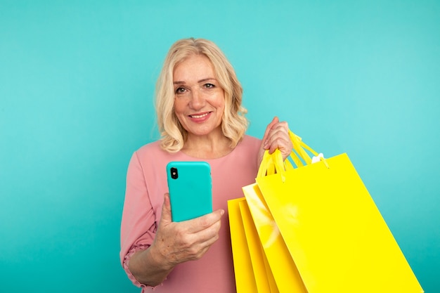 Feliz mujer adulta sosteniendo teléfono y bolsas amarillas.