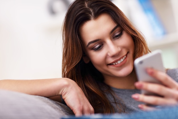 Feliz mujer adulta usando el teléfono en casa en la sala de estar