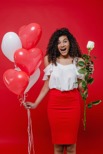 Feliz mujer africana con globos en forma de corazón y rosa blanca