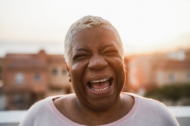 Feliz mujer africana senior sonriendo a la cámara al aire libre en la ciudad - Centrarse en la cara