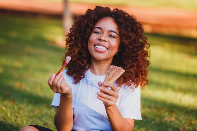 Feliz mujer afro comiendo helado en el parque.