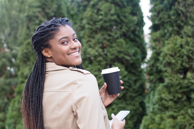 Feliz mujer afroamericana en la calle con café.