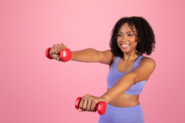 Feliz mujer afroamericana milenaria en ropa deportiva haciendo ejercicios de mano con pesas