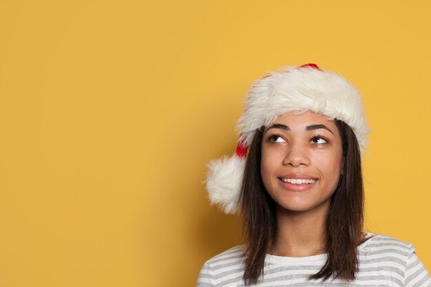 Feliz mujer afroamericana con sombrero de Papá Noel en fondo amarillo