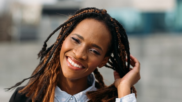 Feliz mujer afroamericana. Sonrisas atractivas del modelo. Mujer sonriente feliz en el enfoque selectivo al aire libre, peinado de moda, concepto de felicidad