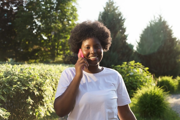 Feliz mujer afroamericana con un teléfono en la calle en verano.