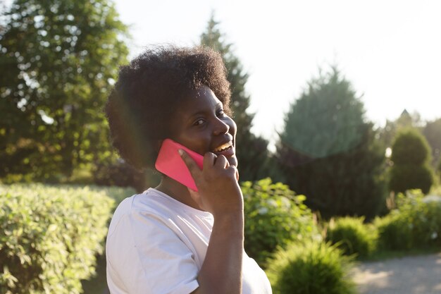 Feliz mujer afroamericana con un teléfono en la calle en verano.