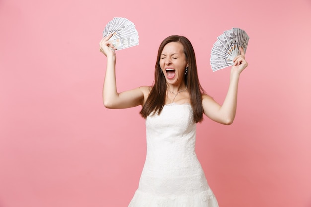 Feliz mujer alegre con los ojos cerrados en vestido blanco mantenga un montón de dólares, dinero en efectivo gritando