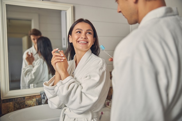 Feliz mujer alegre vistiendo bata blanca de pie en el baño.