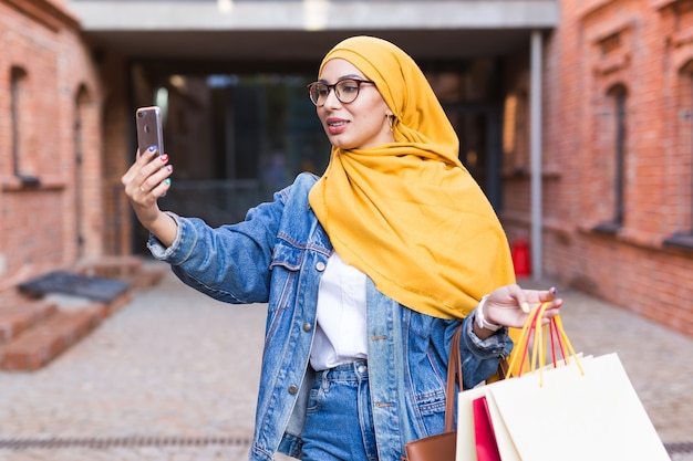 Feliz mujer árabe tomando selfie al aire libre después de ir de compras