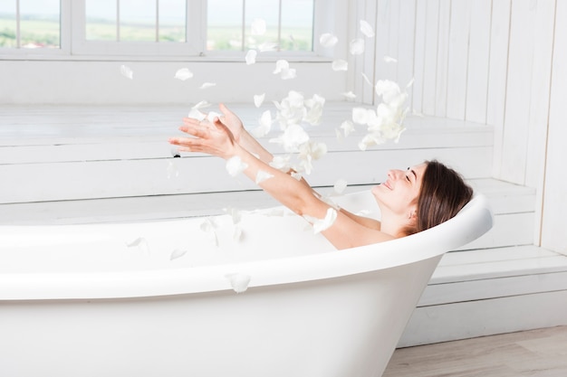 Foto feliz mujer arrojando pétalos en la bañera