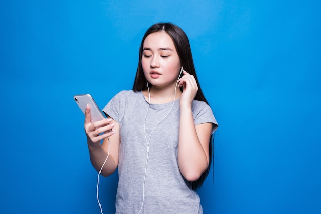 Feliz mujer asiática con auriculares y teléfono inteligente aislado en la pared azul.