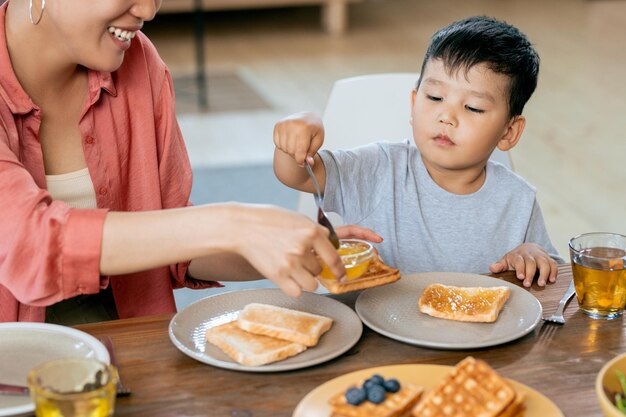 Feliz mujer asiática ayudando a su pequeño hijo a hacer sándwich