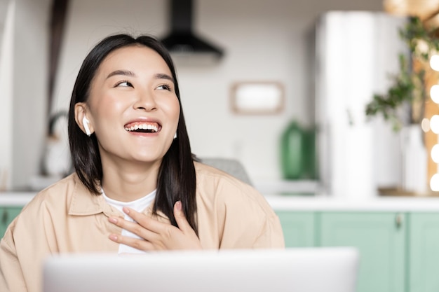 Feliz mujer asiática en casa relajándose con la computadora riendo viendo videos en la computadora portátil