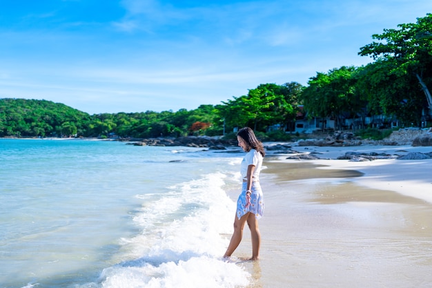 Foto feliz mujer asiática disfruta jugando con las olas del mar en la playa tropical, chica en traje de baño relajarse en las vacaciones de verano en la playa del mar azul en la noche
