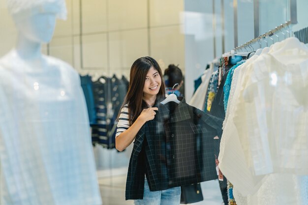 Feliz mujer asiática elegir ropa en tienda de vidrio en el centro del departamento