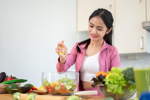 Una feliz mujer asiática está exprimiendo un limón en su ensalada preparando su desayuno saludable en la cocina