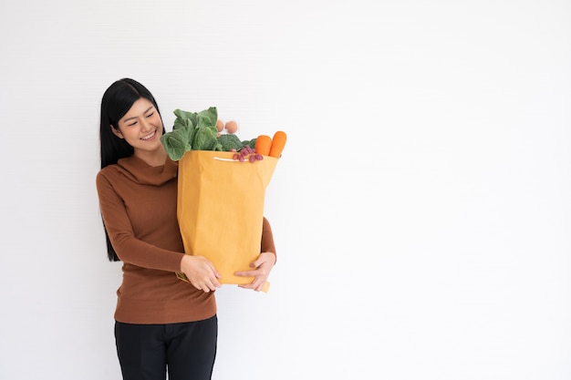 Feliz mujer asiática está sonriendo y lleva una bolsa de papel de compras