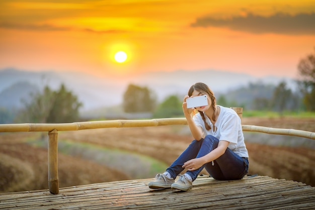 feliz mujer asiática joven tomando teléfono inteligente de forma selfie durante el verano Puesta de sol con paisaje