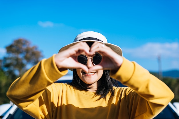 Foto feliz mujer asiática de pie y mostrando las manos en forma de corazón en la naturaleza, feliz y sonriente, pensamiento positivo, vista posterior