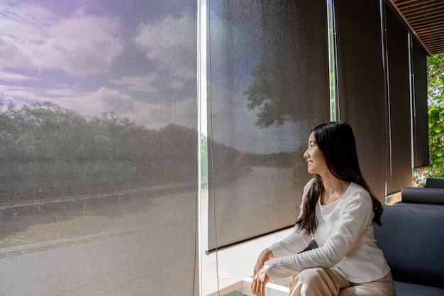 Feliz mujer asiática relajarse con la naturaleza verde a través de la ventana de cristal en casa