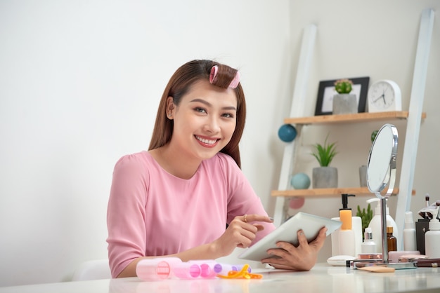 Feliz mujer asiática con rizadores de pelo con tableta en casa