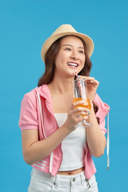 Feliz mujer asiática en ropa casual de verano con un vaso de bebida de jugo de fruta fresca sobre fondo azul.