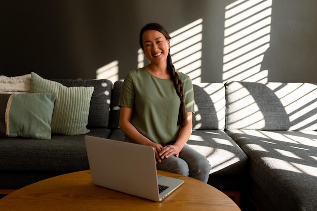 Foto feliz mujer asiática sentada en un sofá en casa y usando una computadora portátil