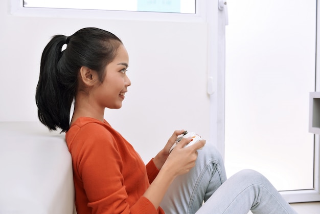 Feliz mujer asiática sentada en el suelo y jugando videojuegos