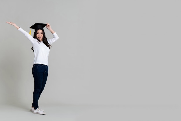 Feliz mujer asiática sonriendo y vistiendo gorra graduada